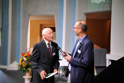 Ein älterer Mann wird in festlichem Rahmen interviewt. 