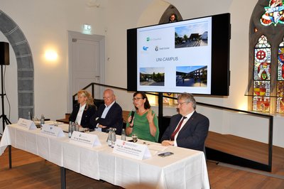 Vier Personen sitzen im Rahmen einer Pressekonferenz an einem Tisch. 