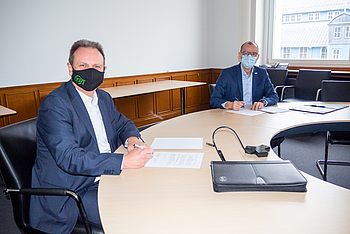 Zwei maskierte Personen unterschreiben ein Dokument