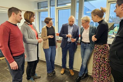 Ein Mann erläutert einer Gruppe einen Forschungsgegenstand, den er in der Hand hält.