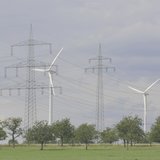 Stromnetze und Windräder in der Landschaft. In das Bild integriert ist ein kleines Porträtfoto eines Mannes.