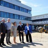 Gruppe von fünf Personen steht repräsentativ vor einem Neubau. 