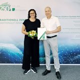 Zwei Personen stehen vor einer Wand mit einem Logo der TU Clausthal.
