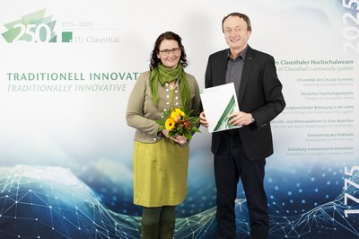 Die Clausthaler Universitätspräsidentin und ein neuer Professor stehen vor einer Wand mit Logo der TU Clausthal.
