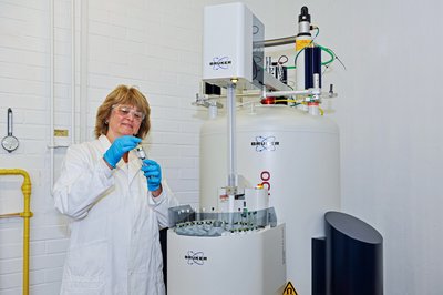 Frau im weißen Kittel und mit Schutzbrille arbeitet an einem Forschungsgroßgerät.