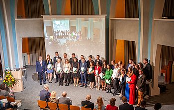 Personen mit Urkunden in der Hand nebeneinander vor einem Projektionsschirm