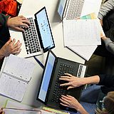 Personen an einem Tisch mit Laptops und Papieren