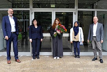 Eine Person mit Blumen in der Hand steht neben anderen vor einem Eingang