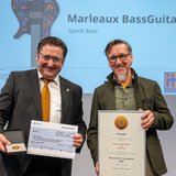 Im Rahmen einer Preisverleihung zeigen zwei Männer einen symbolischen Scheck sowie eine Urkunde.