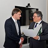 Zwei Personen schütteln sich vor einem Fernseher die Hände