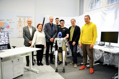 Eine Personengruppe steht mit einem Roboter in einem Labor. 