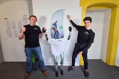 Zwei Männer nehmen einen humanoiden Roboter in die Mitte. 