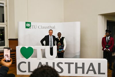 Zwei Menschen posieren vor einem I LOVE TU CLAUSTHAL Schild. 