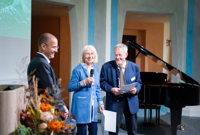 Zwei Männer und eine Frau stehen vor einem Publikum. 