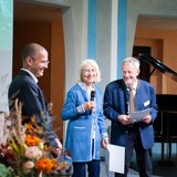 Zwei Männer und eine Frau stehen vor einem Publikum. 