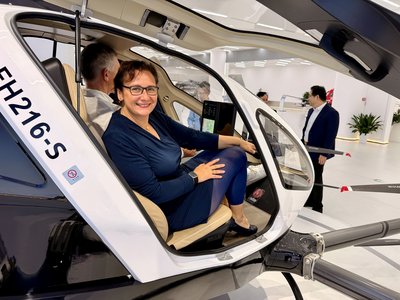 Eine Frau sitzt in einem kleinen Hubschrauber, der noch am Boden steht. 