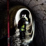 Eine Gruppe wandert durch einen Stollen, der zum Teil mit Wasser gefüllt ist.