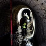 Eine Gruppe wandert durch einen Stollen, der zum Teil mit Wasser gefüllt ist.