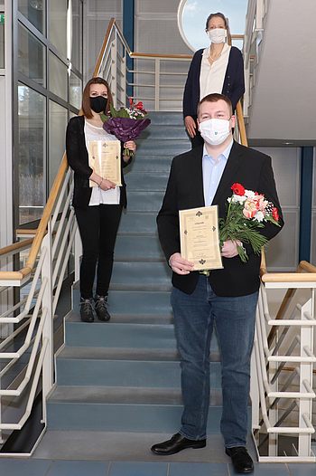 Menschen mit Blumen halten eine Urkunde und stehen auf einer Treppe 