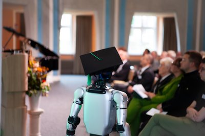 Ein humanoider Roboter, der einen Doktorhut trägt, läuft vor einem Publikum auf. 