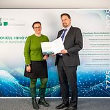 Die Präsidentin steht mit Prof. Keszöcze, der seine Urkunde hält, vor einer Fotowand