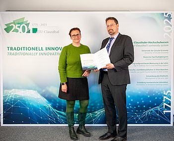 Die Präsidentin steht mit Prof. Keszöcze, der seine Urkunde hält, vor einer Fotowand
