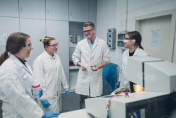 Vier Personen mit Laborkitteln und Schutzbrillen in einem Labor