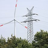 Elektrischer Mast mit einer Windturbine im Hintergrund