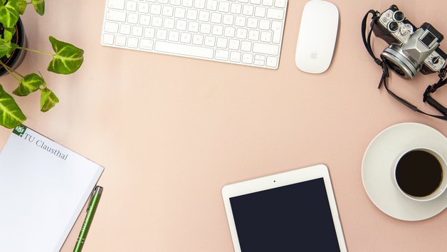 Schreibtisch mit Tastatur, Maus, Block, Stift, Tablet, Kamera und Kaffee