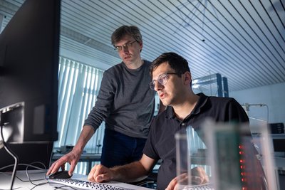 Zwei Männer, einer sitzend, einer stehend, schauen in einer Laboratmosphäre auf einen Bildschrim.