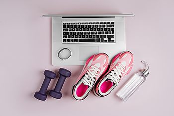 Schuhe, Hanteln, Uhr, Wasserflasche neben einem Laptop
