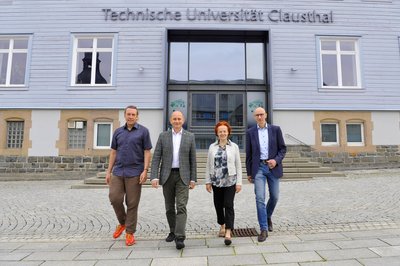 Vier Personen laufen im Gleichschnitt vor dem Hauptgebäude der Technischen Universität Clausthal entlang.