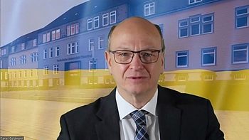 Eine Person bei einer Präsentation mit der ukrainischen Flagge und dem Hauptgebäude der TU Clausthal im Hintergrund