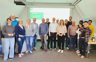 Eine Gruppe von 15 bis 20 Personen steht vor einer Leinwand.
