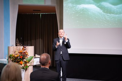 Ein Mann hält vor Publikum eine Rede. 